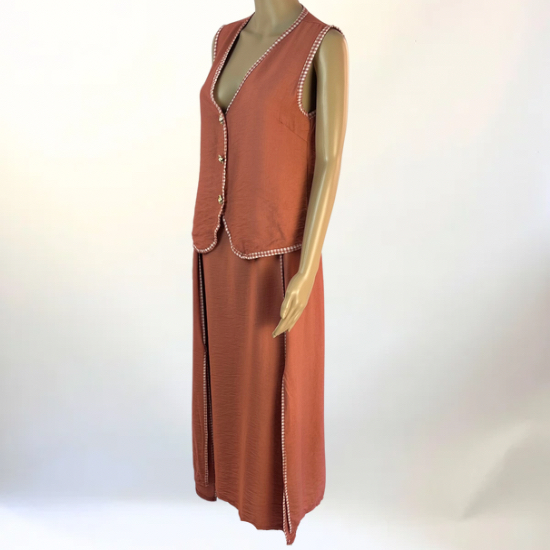 La imagen muestra un conjunto de dos piezas en color verde, compuesto por un chaleco sin mangas con botones decorativos en la parte frontal y una falda larga con abertura lateral. El diseño es elegante y versátil, ideal para ocasiones casuales o semi-formales. El tejido ligero y transpirable garantiza comodidad y un ajuste favorecedor.
